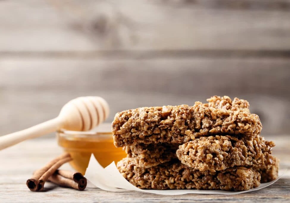 Tasty granola bars with honey in bowl and cinnamon on wooden table